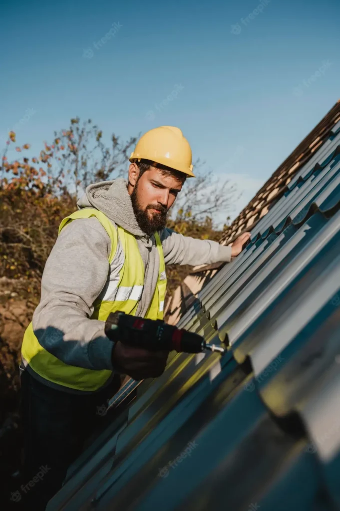Roofer in a hard hat fastening a metal roofing panel