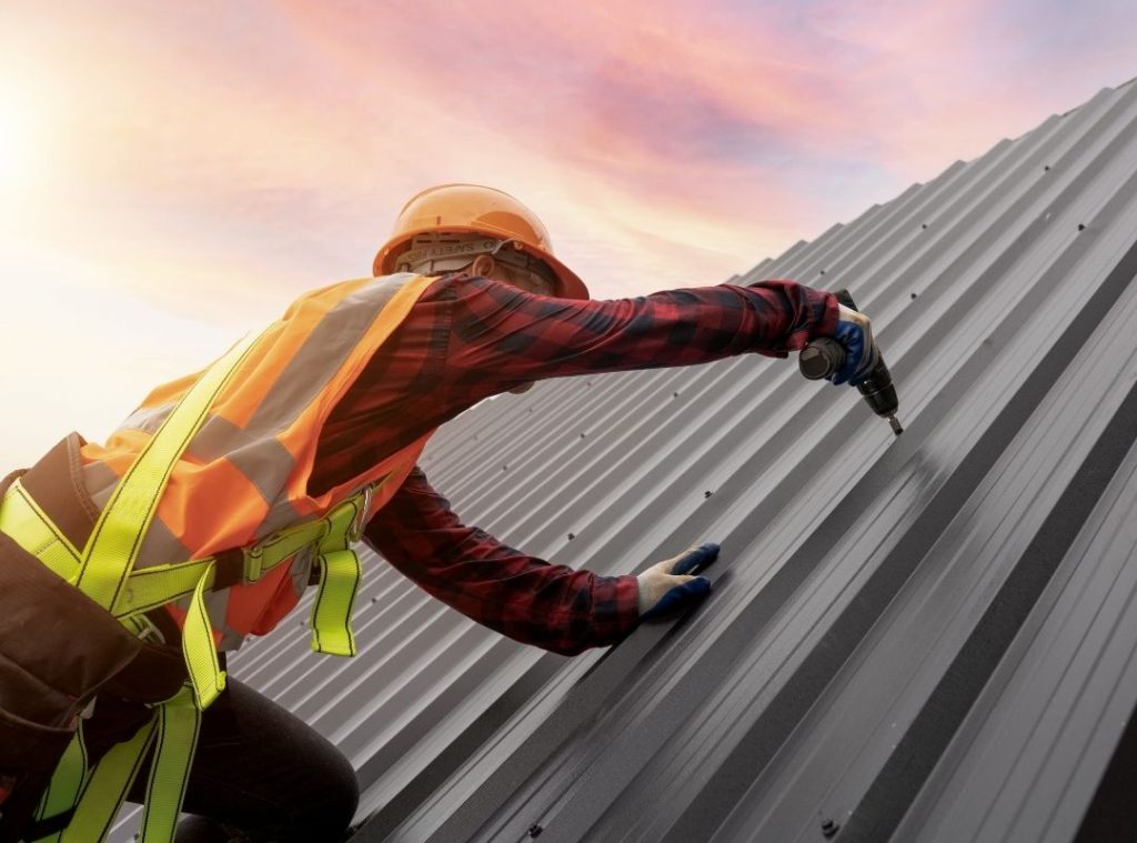 Roofer in high visibility clothing fastening panels on a metal roof
