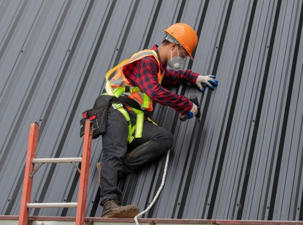Roofer working on a corrugated metal roof beside a ladder