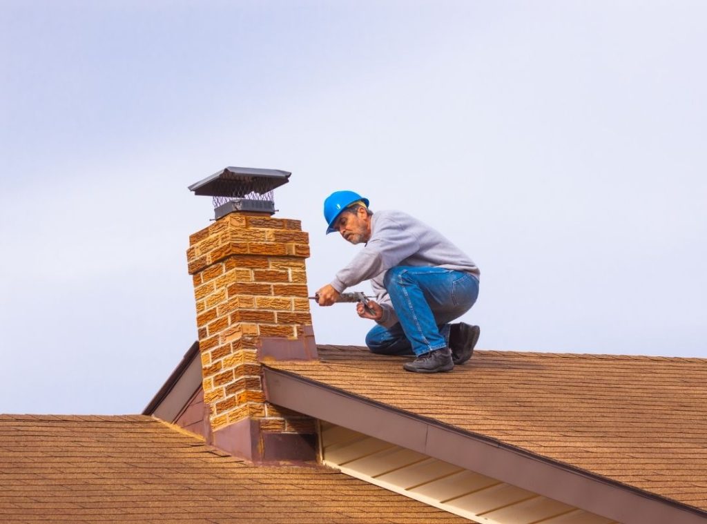 Roofer sealing the flashing around a brick chimney