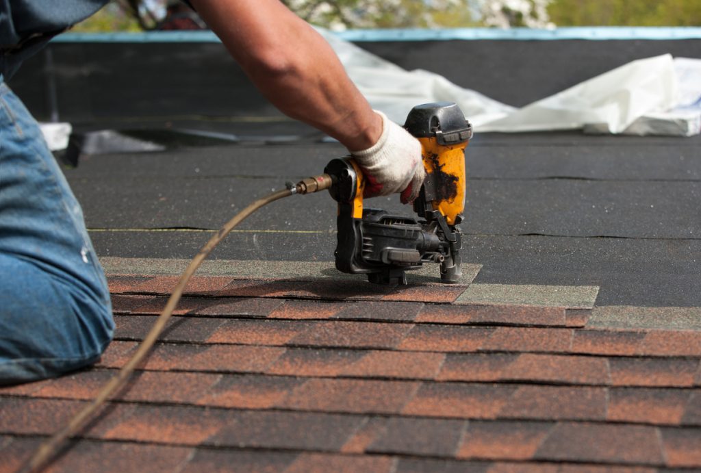 Roofer using a nail gun to fix shingles
