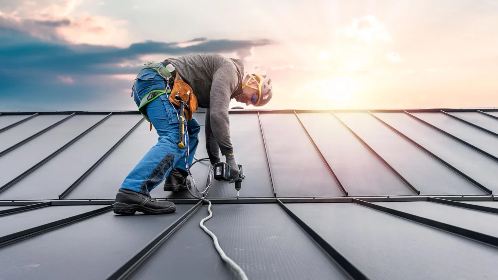 Roofer fixing panels on a metal roof at sunset