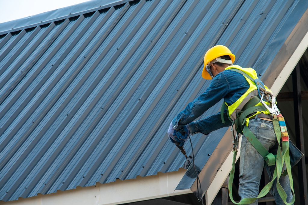 Roofer in a safety harness on a dark metal roof
